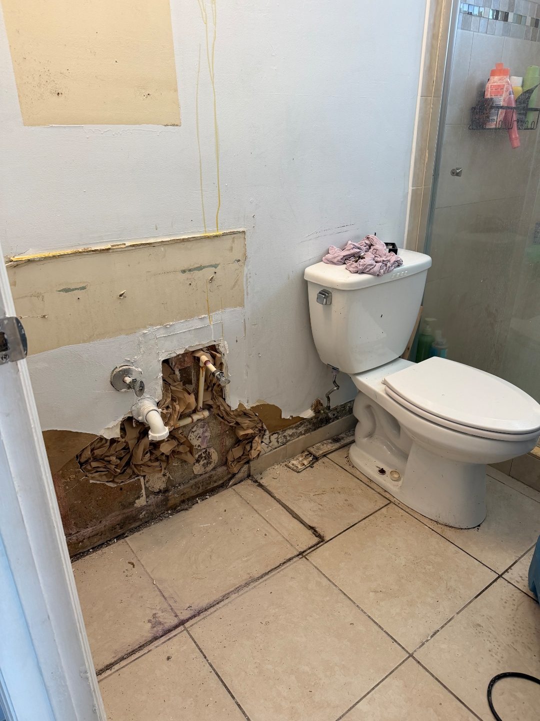 Bathroom corner showing an open wall section with exposed plumbing beside a toilet