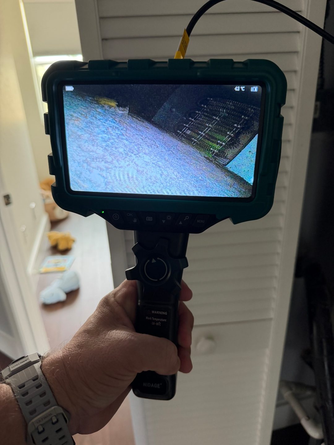 Hand holding a borescope camera near a closet door, a second angle of the same coil-pattern scan