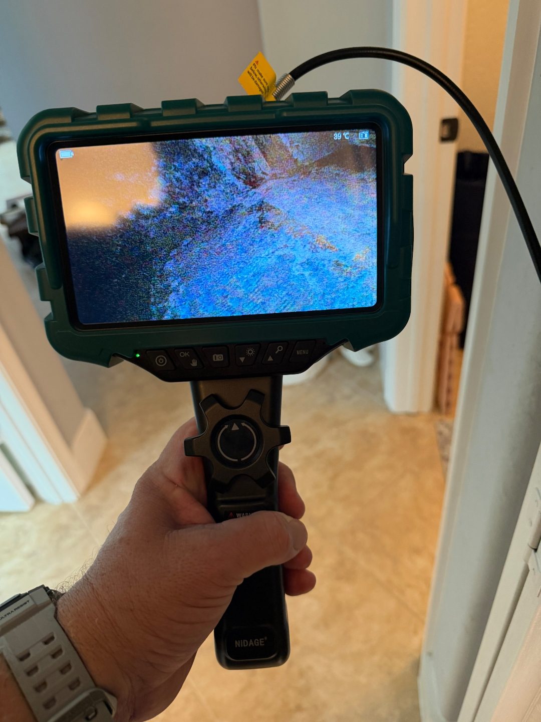 Hand holding a borescope camera with its screen showing a close up scan in a hallway