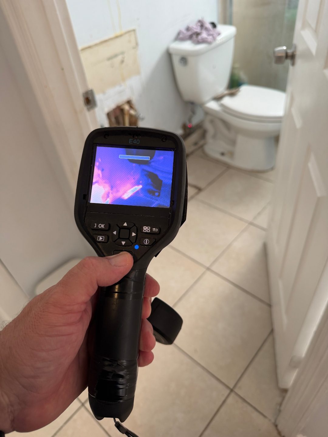 Hand holding a thermal imaging camera near an open bathroom wall section from a different angle