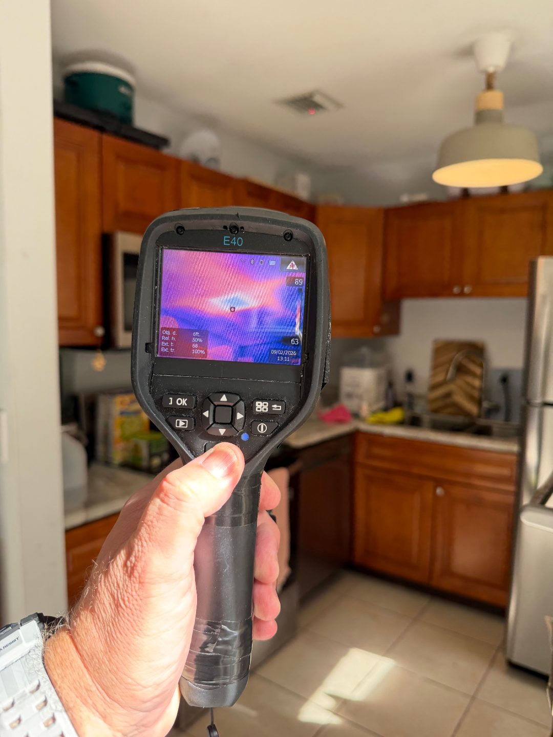 Hand holding a thermal imaging camera displaying a heat map scan in a kitchen