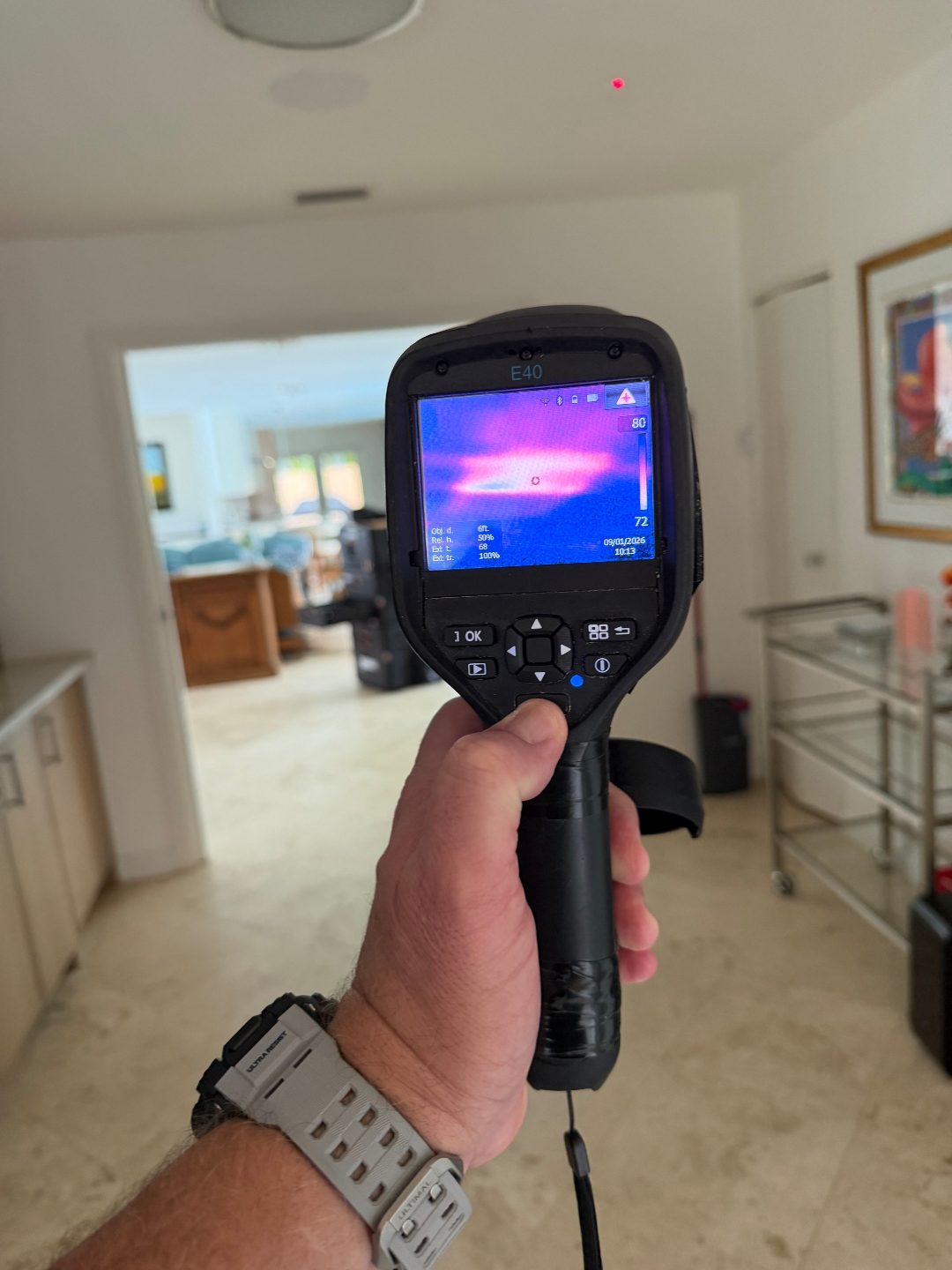 Hand holding a thermal imaging camera displaying a scan in an open-plan hallway area
