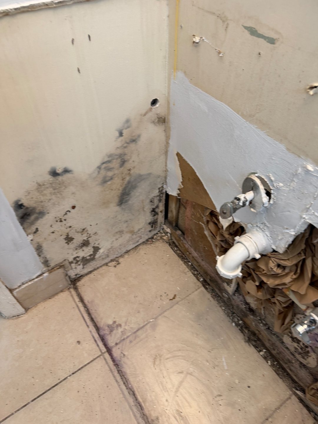 Close-up of a wall corner with staining and an adjacent section of exposed plumbing
